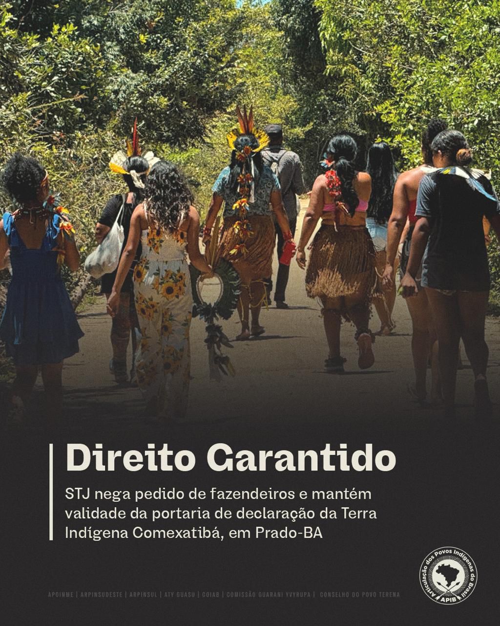 Card informativo com uma fotografia de um grupo de pessoas indígenas caminhando por uma estrada cercada por vegetação densa. Algumas pessoas usam cocares de penas, saias de fibras vegetais, adornos tradicionais e carregam objetos cerimoniais, enquanto outras vestem roupas casuais. A imagem é vista por trás do grupo, que segue em direção ao interior da mata. Na parte inferior, sobre um fundo escuro, aparece o título em destaque "Direito Garantido". Abaixo, lê-se: "STJ nega pedido de fazendeiros e mantém validade da portaria de declaração da Terra Indígena Comexatibá, em Prado-BA". No canto inferior direito está o logotipo da Articulação dos Povos Indígenas do Brasil (APIB), e na base do card aparecem os nomes de organizações indígenas apoiadoras.